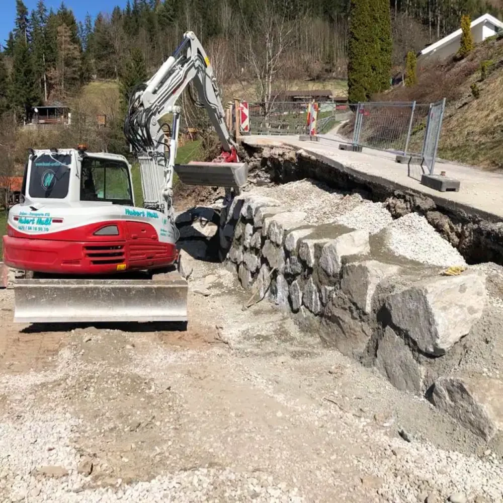 Kettenbagger von Hussl Erdbau führt Arbeiten an einer Steinmauer durch